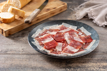 Spanish serrano ham slices on black plate on wooden table