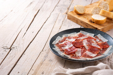 Spanish serrano ham slices on black plate on wooden table. Copy space
