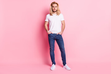 Full length photo of positive happy young man hold hands pockets good mood isolated on pink color background