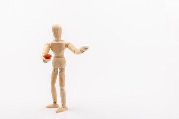 A wooden Gestalta doll or mannequin holds red and white pills in its hands on light background. The concept of choice.