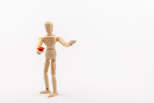 A wooden Gestalta doll or mannequin holds red and white pills in its hands on light background. The concept of choice.