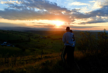 A young couple climbing a hill watching the beautiful sunset and landscape in the distance