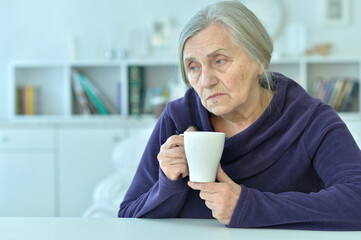 Portrait of a sad old woman drinking tea