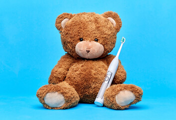 dental care, health and childhood concept - brown teddy bear with electric toothbrush over blue background