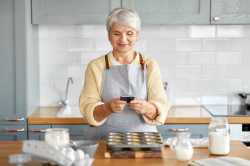cooking, food and culinary concept - happy smiling senior woman with smartphone taking picture of...
