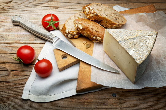 Cow's milk caciotta, Formaggella bergamasca. Rustic snack with Italian cheese, cherry tomatoes and wholemeal bread with cutting board and knife on old wooden background.