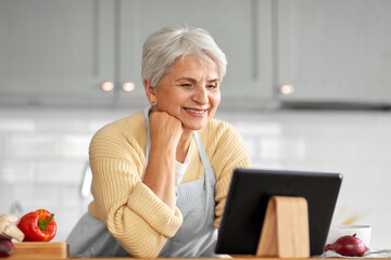 healthy eating, food cooking and culinary concept - happy smiling senior woman with tablet pc computer and vegetables on kitchen at home