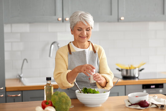 healthy eating, food cooking and culinary concept - happy smiling senior woman with salt making vegetable salad on kitchen at home
