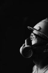 Profile portrait miner in helmet, respirator and goggles, looking at light.Dirty worker in shirt.