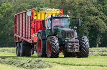 Picking up dried grass for silage with a green tractor and red loader wagon.