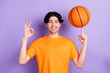 Photo of cheerful young positive man show okay sing spin basketball finger sport isolated on violet...