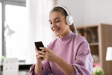 technology and people concept - happy smiling girl in headphones with smartphone at home