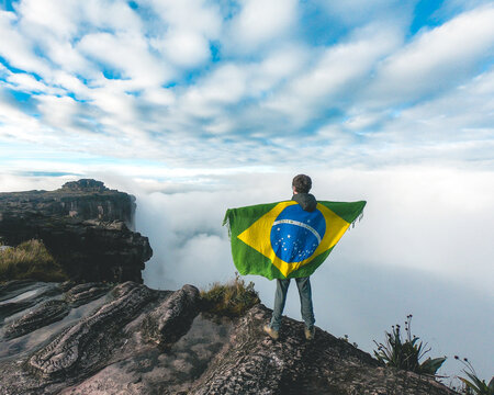 homem não identificado segurando bandeira do brasil no topo do Monte Roraima, com mar de nuvens ao fundo