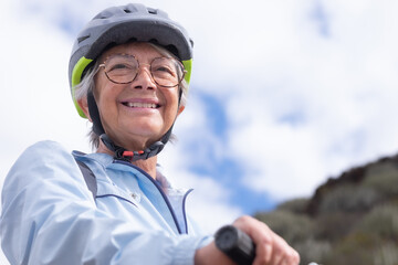 Portrait of smiling senior biker woman wearing sport helmet and eyeglasses in outdoors excursion