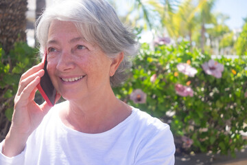 Attractive elderly woman smiling talking with mobile phone outdoors in a green public park