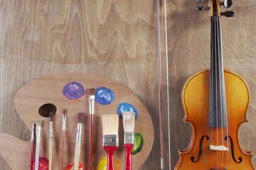 Attributes of the arts. Painting, music. Art palette, brushes, violin on a wooden textured background.