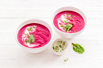 Two white bowls of red beet soup with sour cream and green herbal salt