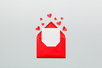 Red paper envelope with empty white card and heart on colored background. top view valentines day concept