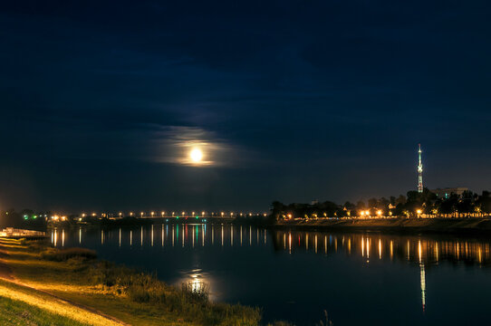 Tver, Volga river night moonlight landscape, evening city beautiful scenery. Moon in clouds view, night lights reflections in water