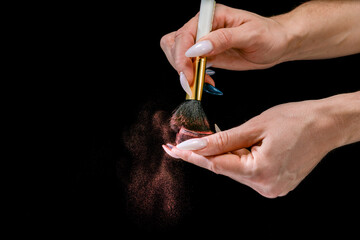 A girl with a long manicure applies red powder to a brush. Small particles of powder are all around. close-up