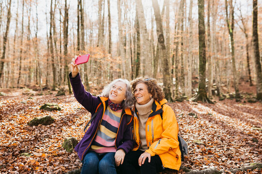 Two senior female taking a selfie after hiking together through the forest in autumn