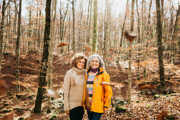 Two senior female friends hiking together through the forest in autumn