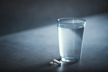 Glass of fresh water and medicine on a dark table. Daily routine of drinking and eating pills. 