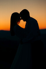 Groom and bride stand on the mountain against the background of sunset
