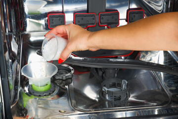 Adding salt to the dishwasher. A woman's hand pours salt to soften the water into the dishwasher. Dishwasher salt for regenerating the water softener