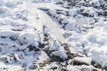 Fototapeta na wymiar Frozen mud under a layer of fresh snow. Close-up of a bad suburban dirt road. Selective focus