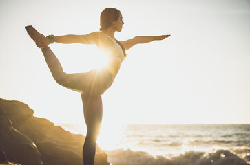 Image of a beautiful young woman making yoga training and meditation on the beach and rocks at...