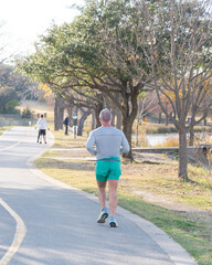 Fototapeta premium Rear view senior man in long sleeve shirt and short running on sidewalk near White Rock Lake park in fall season Dallas, Texas