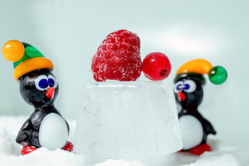 Pair of penguins made from glass in front of raspberry and currant on the ice.