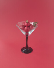 The concept of celebrating the New Year. A martini glass with shiny red Christmas balls and a sprig of spruce on a red background.