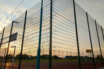 Outdoors mini football and basketball court with ball gate and basket surrounded with high protective fence.