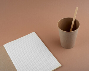 Blank notebook and disposable kraft paper cup on brown background. Free space for your brand