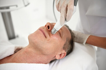 Rejuvenating facial treatment. Mature man getting lifting therapy massage in a beauty SPA salon....
