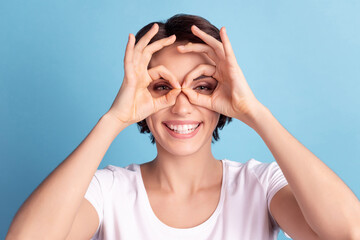 Photo of young cheerful lady have fun show fingers binoculars symbol look isolated over blue color background