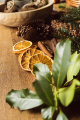 DIY Christmas wreath making on wooden tabletop with evergreen tree branches and dry fruits oranges and pine cones