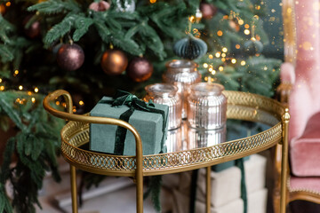 Golden cart with present gift boxes near Christmas tree decorated with handmade eco paper balls.