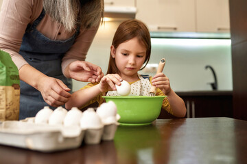 Girl breaking egg during cooking with grandmother