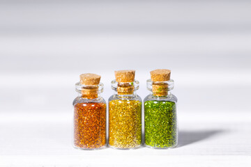 Small Glass jars with golden, orange and green glitters for nail art and makeup on white background, Copyspace