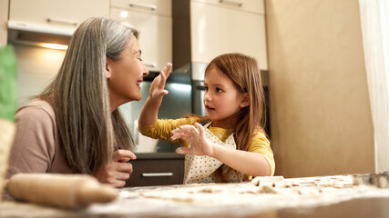 Obraz na płótnie Canvas Little girl touch face of grandmother with flour