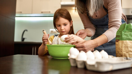 European little girl breaking egg near grandmother