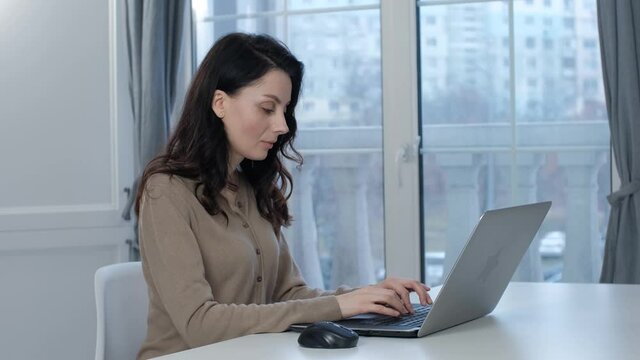 Freelancer woman communicating with client through internet. Free lancer worker working from home. Stock video of pretty brunette model in 30s typing text on laptop computer keyboard