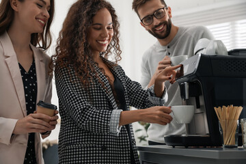 African American woman talking with colleagues while using modern coffee machine in office