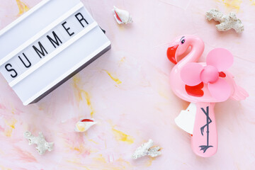 Abstract summer background with text SUMMER seashells and hand flamingo fan on pink. Lifestyle, planning sea vacation, summer holidays concept. Flat lay, top view, copy space