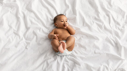 Teething. Little African American baby lying on bed at home