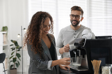 African-American woman talking with colleague while using modern coffee machine in office