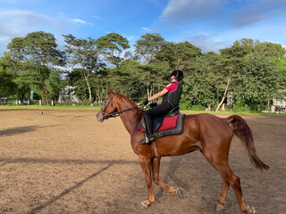 A child wearing Horse riding protective gear riding a brown horse in a ranch